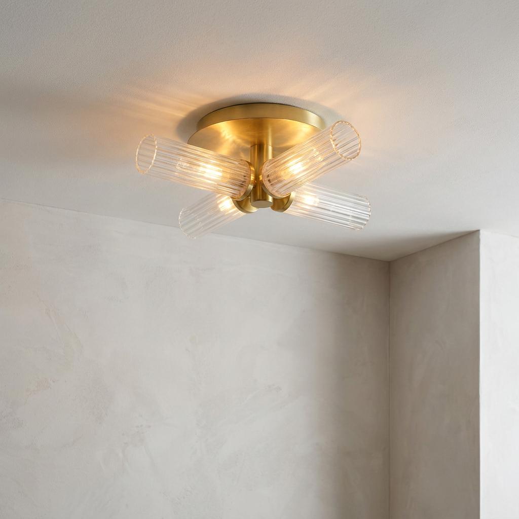 A brass semi-flush ceiling light with four ribbed glass cylinders radiating warm light against a neutral ceiling.