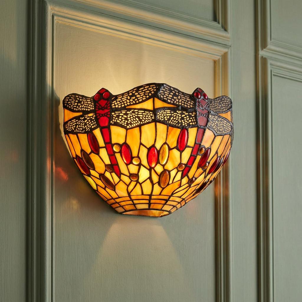 Glowing Tiffany-style wall light featuring red dragonflies on amber stained glass, mounted on a green paneled wall.