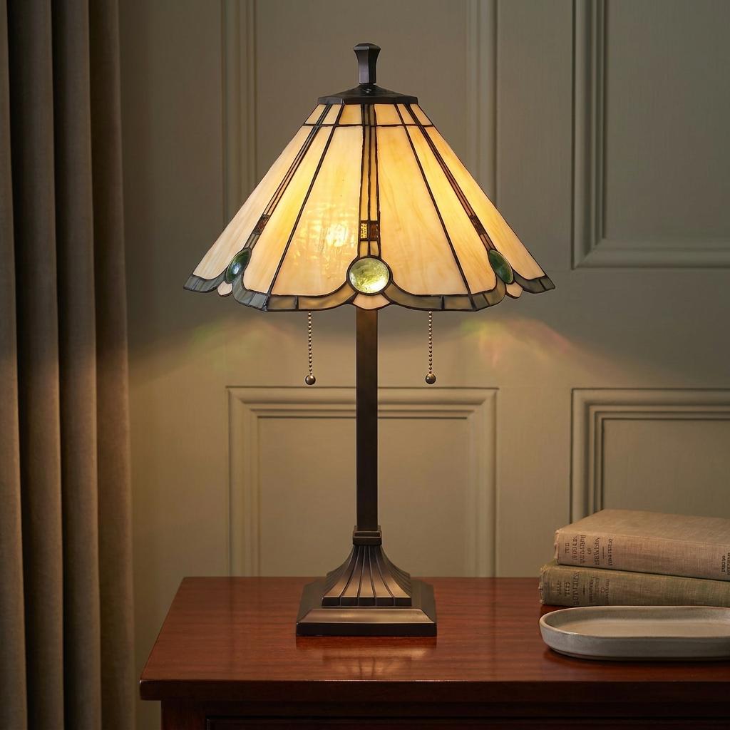 Illuminated Tatton Tiffany table lamp with a cream and green stained-glass shade on a wooden desk.