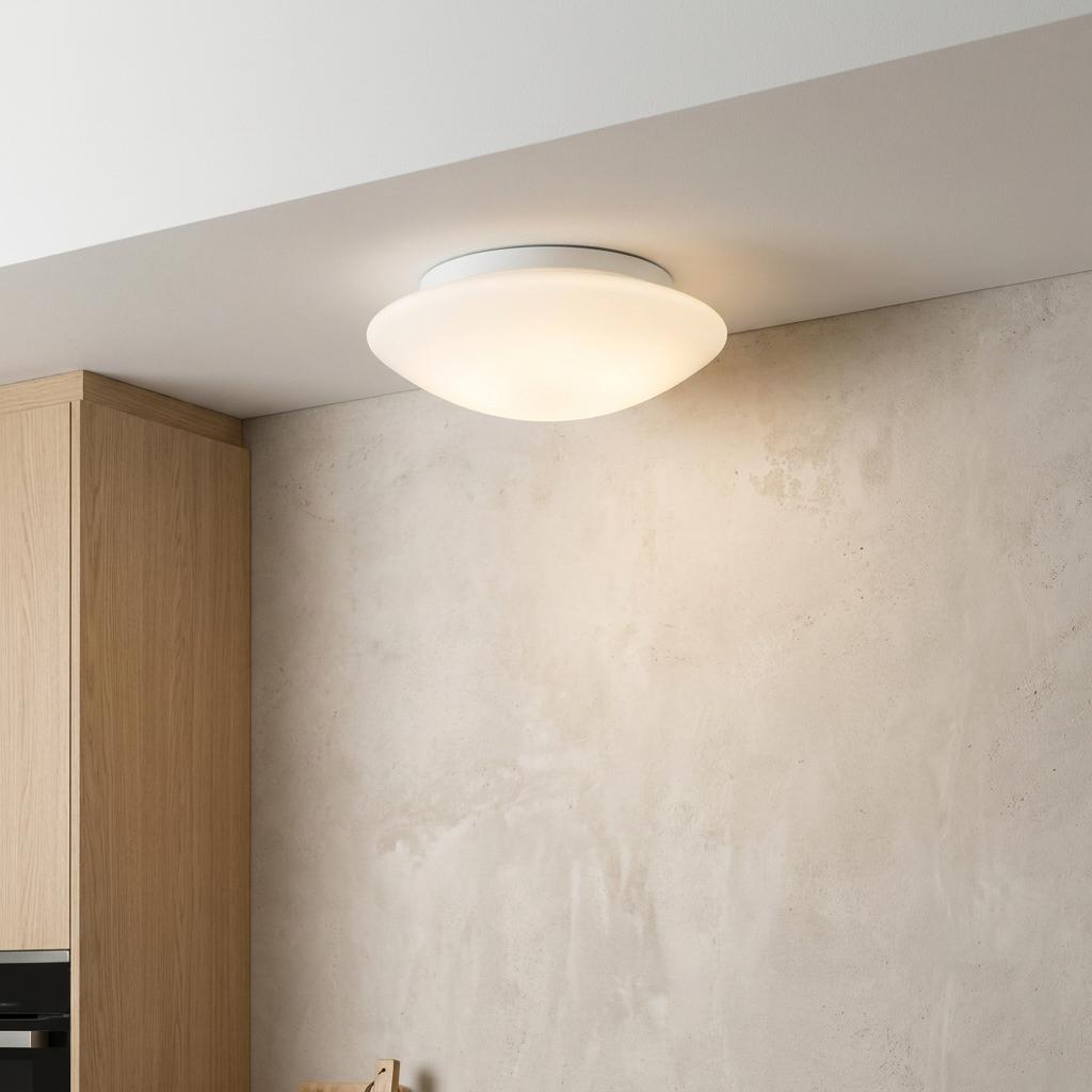 Tokyo white opal glass ceiling flush light illuminated in a modern interior with a textured wall and wood cabinet.