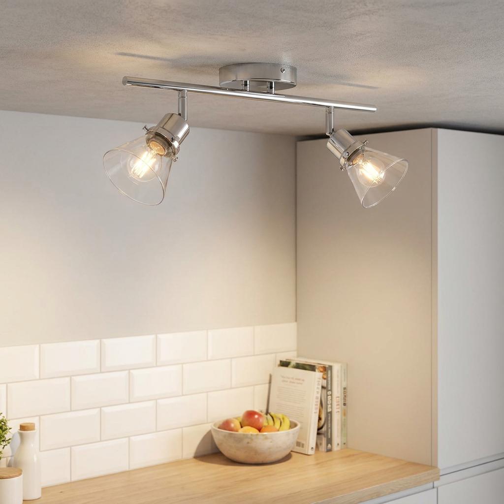 Modern chrome twin bar spotlight with glass shades illuminated above a kitchen counter with white subway tiles.