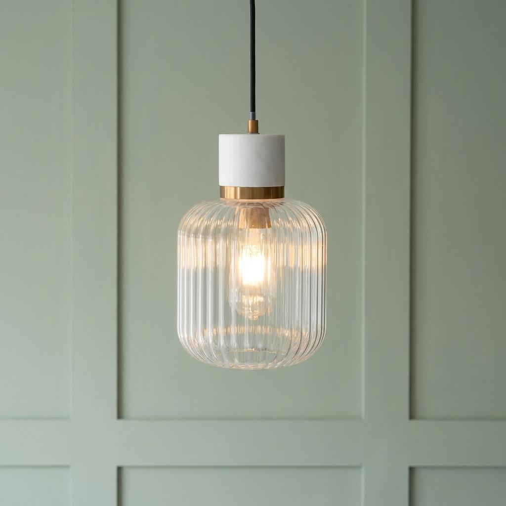 Ribbed glass pendant light with marble and brass details against a sage green paneled wall.
