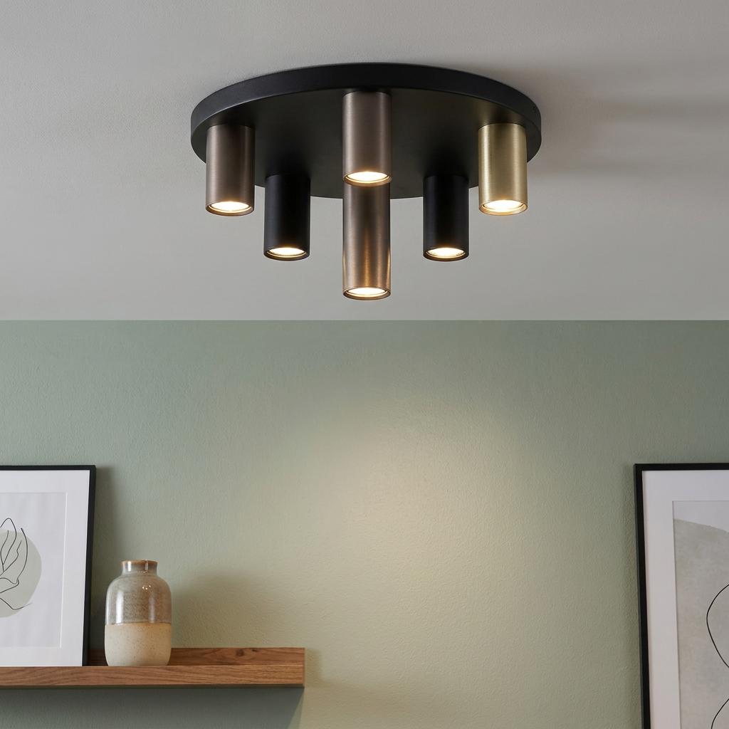 Modern 6-light flush ceiling fixture with mixed black, bronze, and brass tubes illuminating a green wall.
