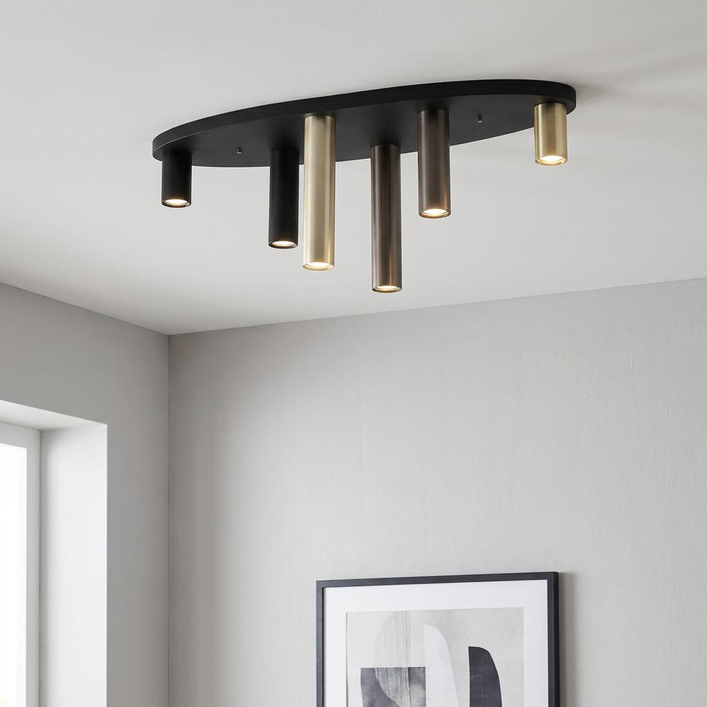 Modern flush ceiling light with multi-colored metallic tubes on a black oval base against a gray wall.