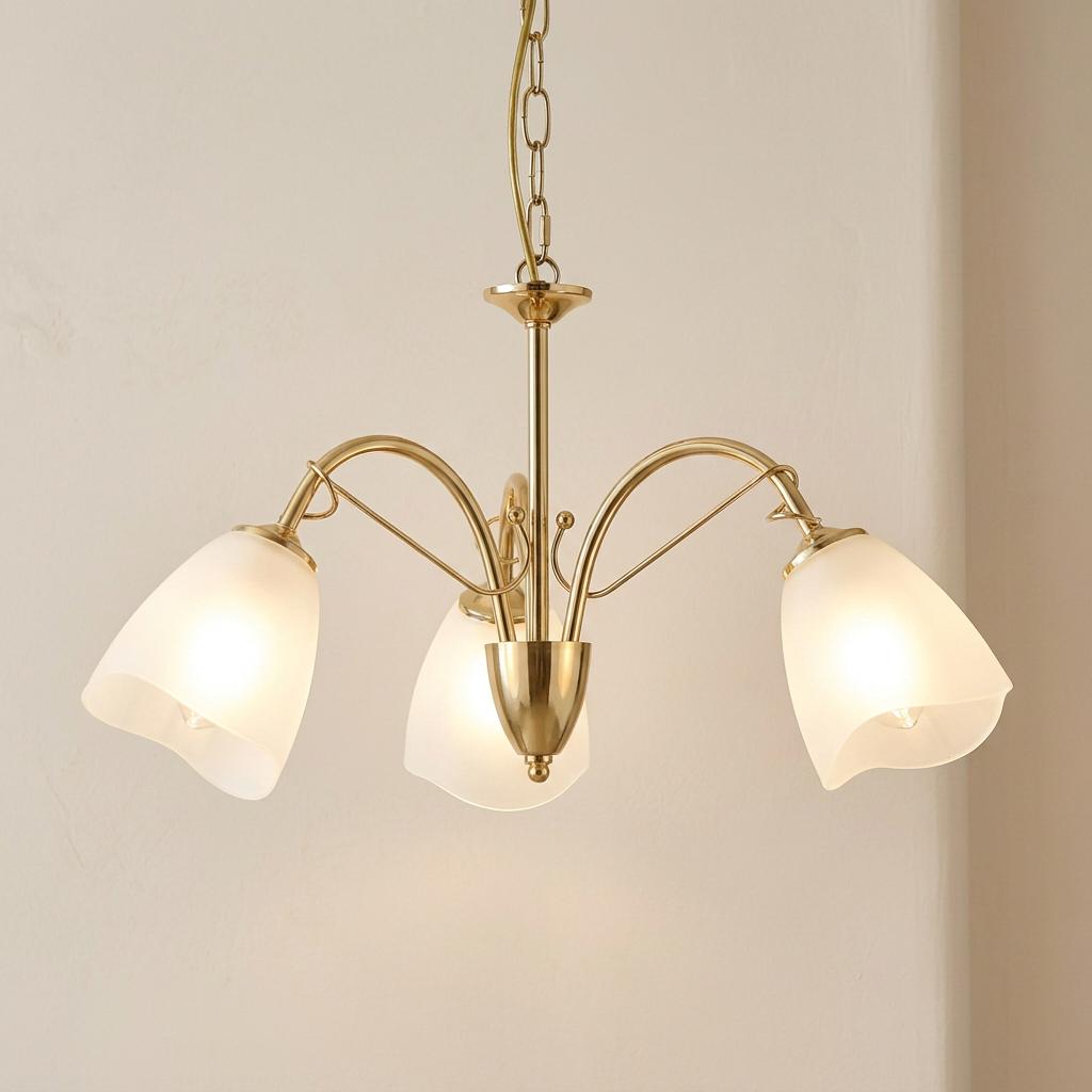 Polished brass 3-light chandelier with frosted glass tulip shades glowing against a cream wall.