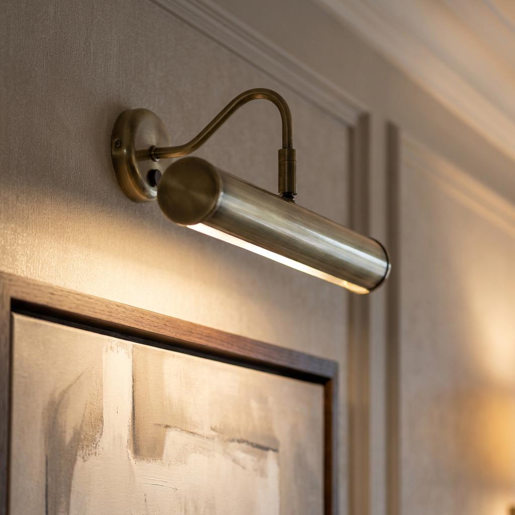 Turner 355mm antique brass picture light illuminating a framed abstract painting on a neutral wall.
