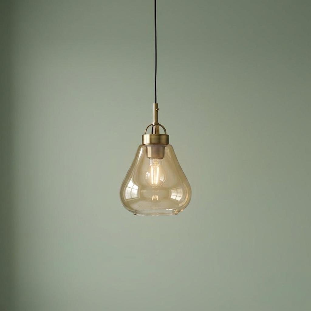 Turua antique brass pendant light with a teardrop amber glass shade hanging against a sage green wall.