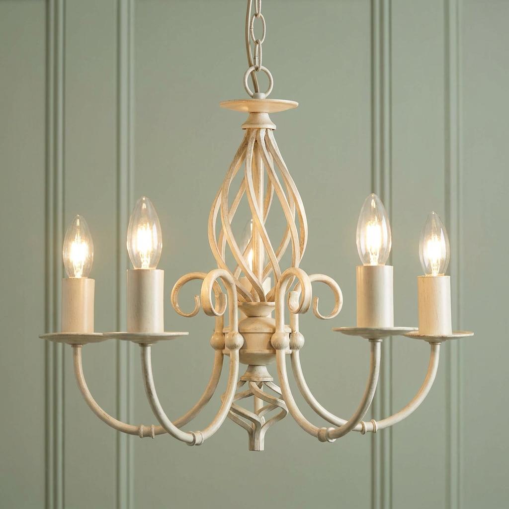 Tuscany Ivory Finish 5 Light Chandelier with candle bulbs and scroll details against a green paneled wall.