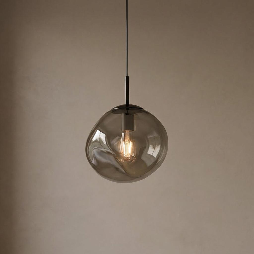 Illuminated twisted sphere smoked glass pendant light with a filament bulb against a minimalist beige wall.