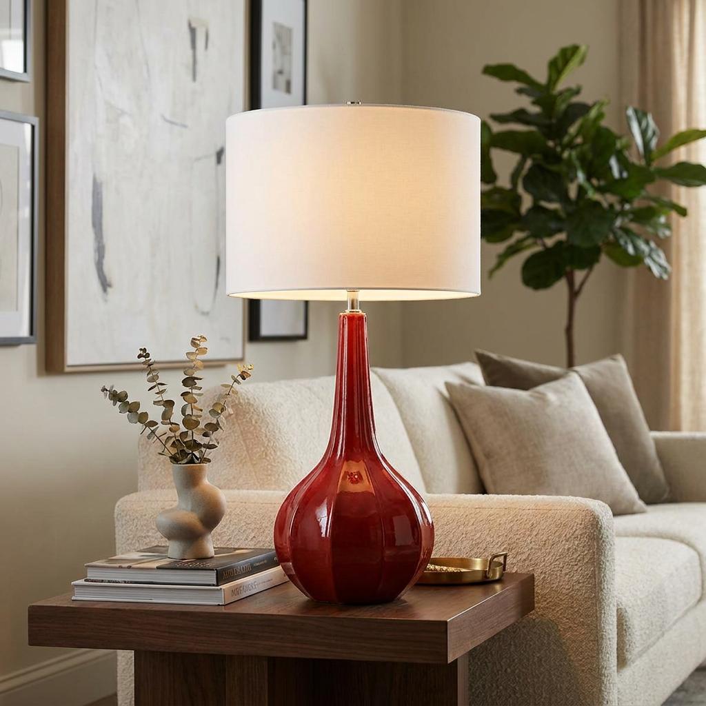 Upton Large Red Ceramic Table Lamp with a white drum shade on a wooden side table in a modern living room.