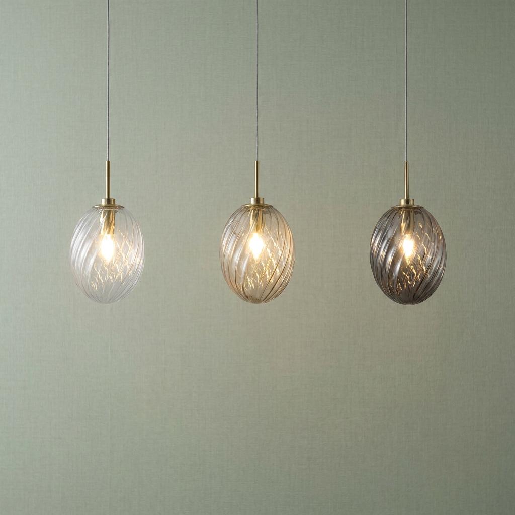 Three pendant lights with swirled glass shades in clear, amber, and smoke grey hanging against a sage green wall.