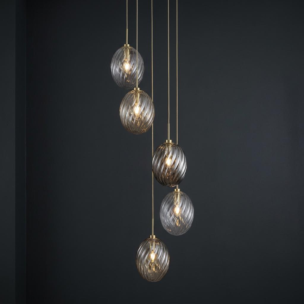 Five cascading swirled glass globe pendants with satin brass fittings hanging against a dark charcoal wall.