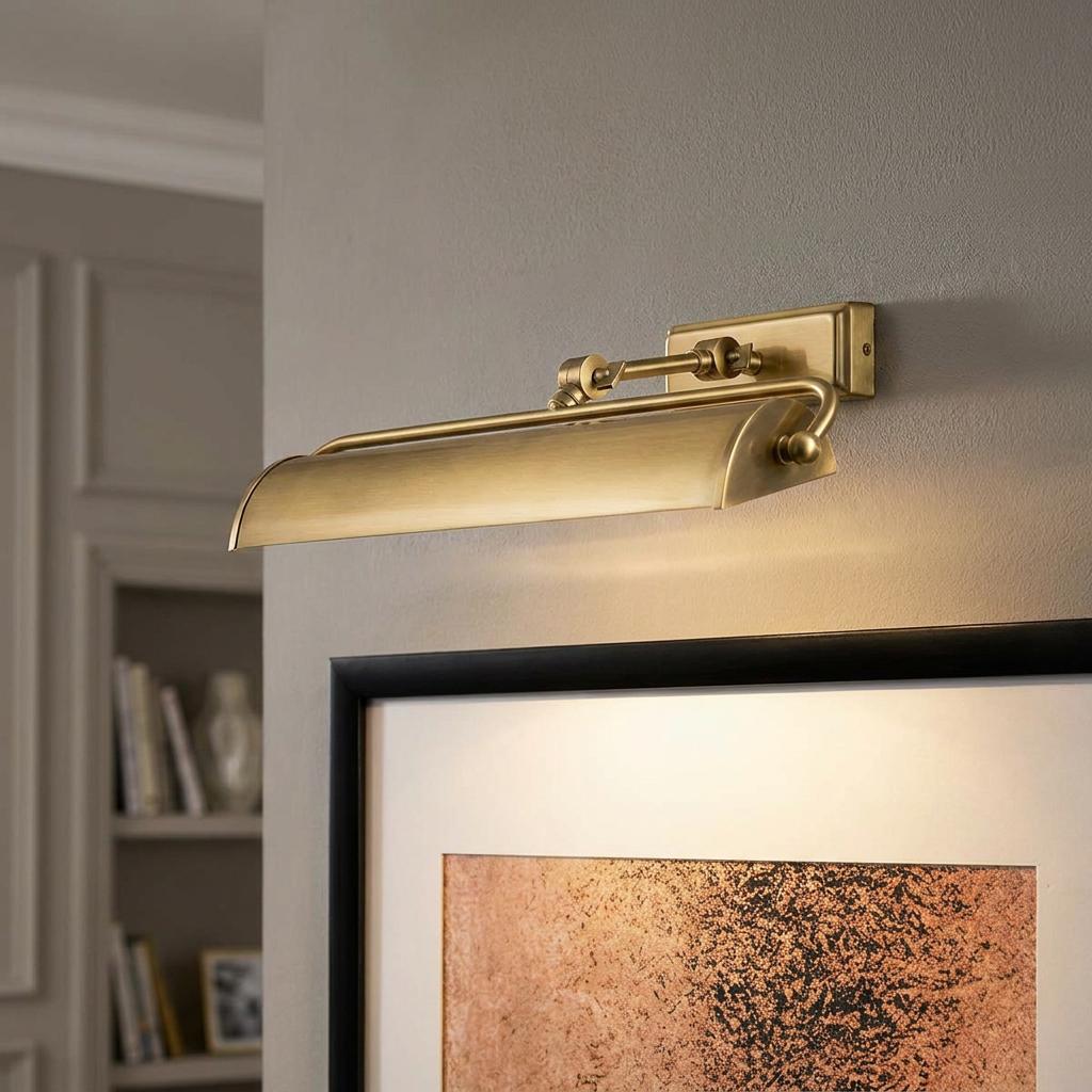 Winchfield brass picture light mounted on a wall above framed art, casting a warm downward glow.