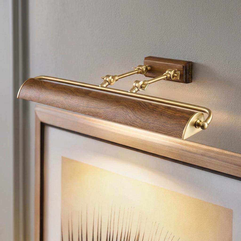 Brass and oak effect picture light mounted on a grey wall, illuminating a framed piece of artwork with a warm glow.