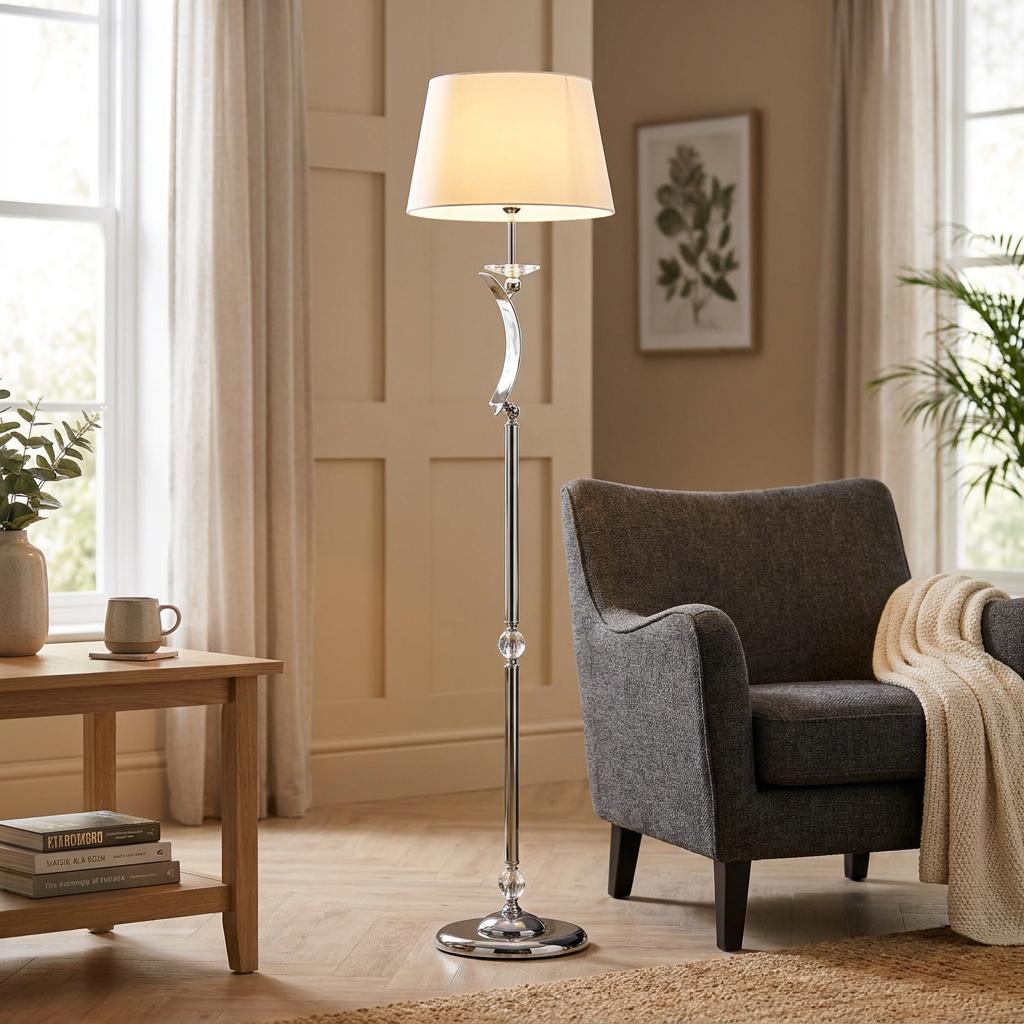 Elegant chrome Wroxton floor lamp with a white shade standing next to a grey armchair in a living room.