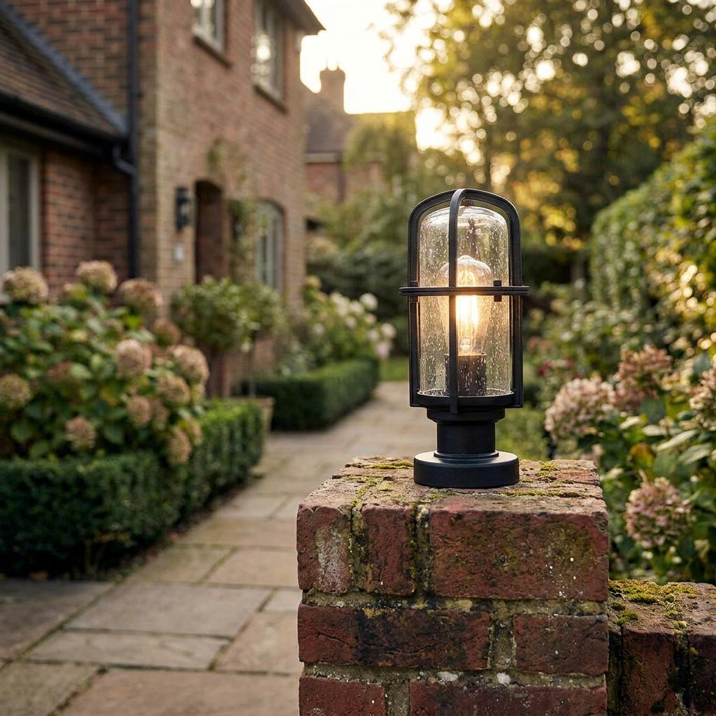 Industrial style black garden lantern with seeded glass mounted on a brick pillar illuminating a stone path.
