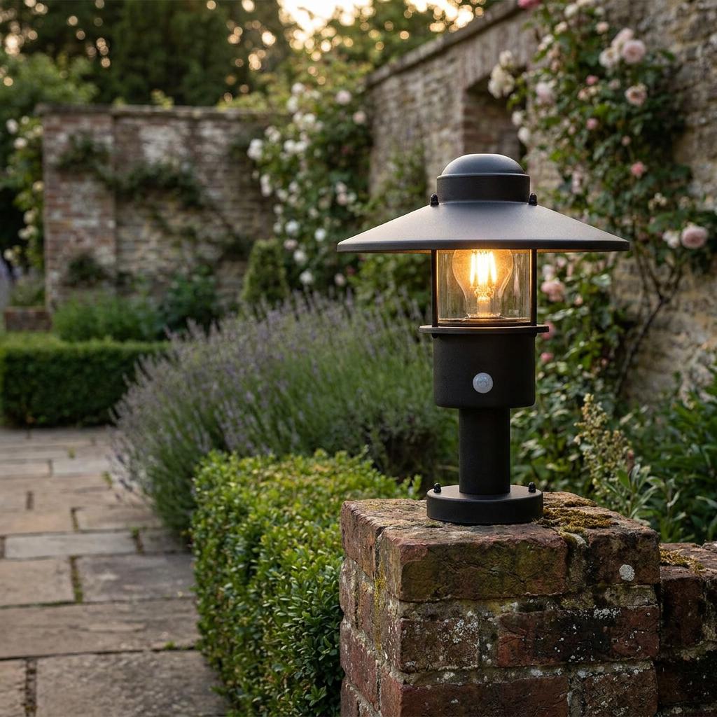 Black outdoor pedestal light with wide flat shade and PIR sensor lit on a weathered brick wall in a garden.