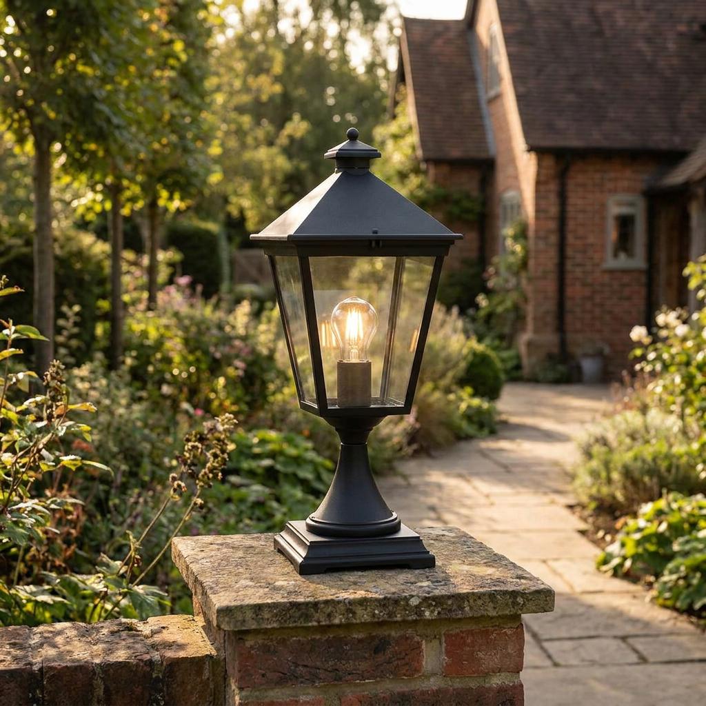 Black traditional lantern light mounted on a brick pillar in a garden pathway.