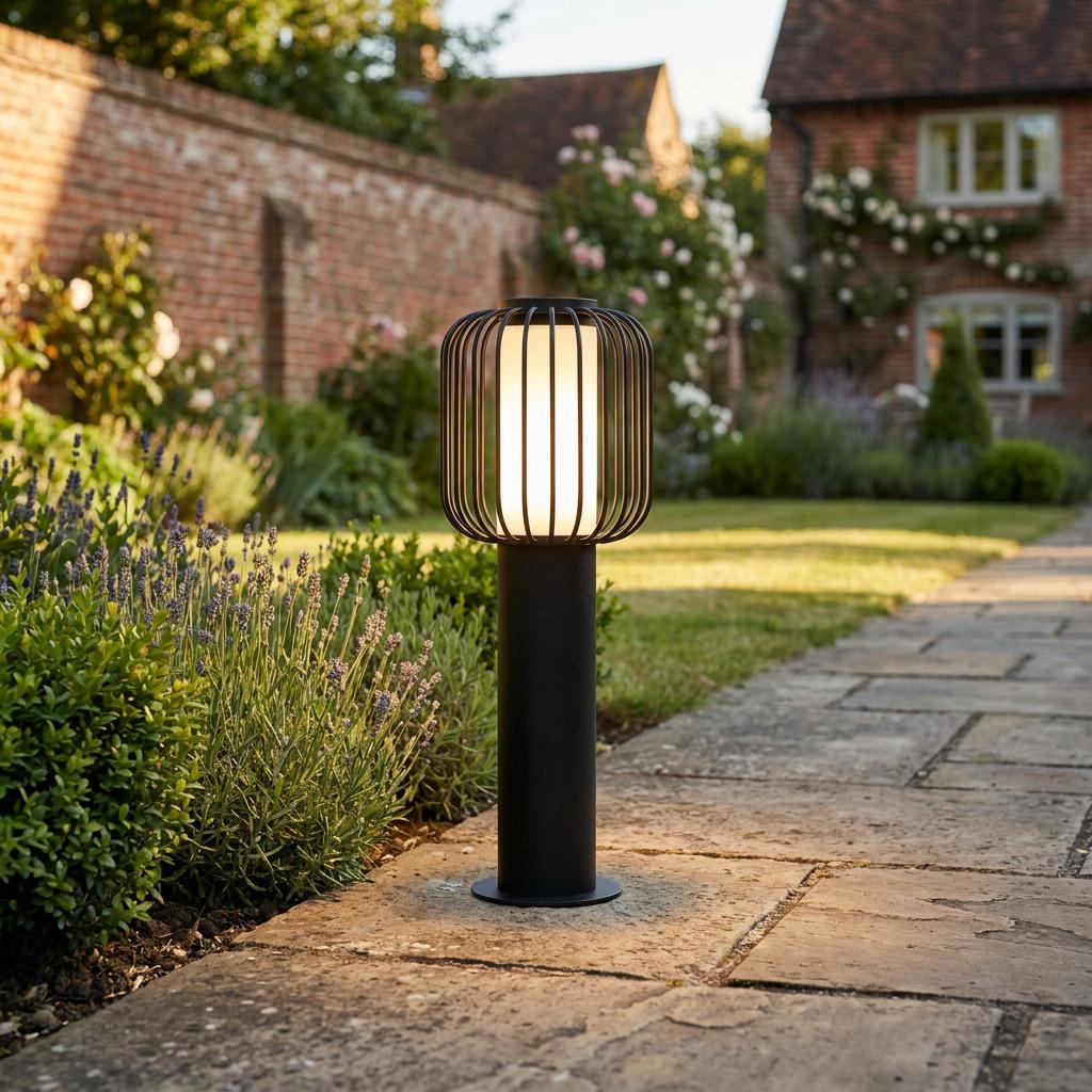 Contemporary black metal cage bollard light illuminating a stone garden path at sunset.
