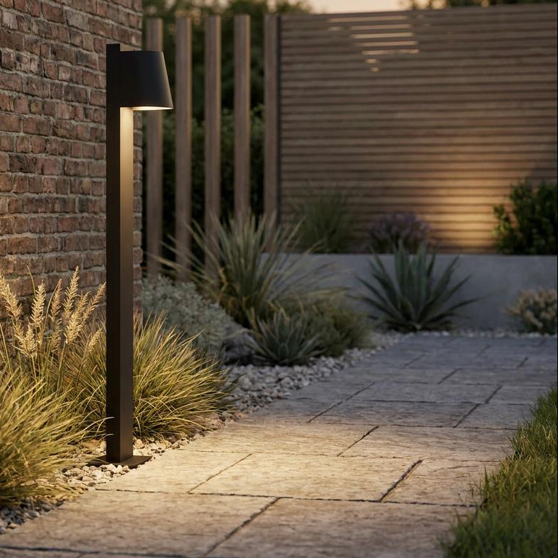 Modern black wall-mounted sconce and bollard light illuminating a brick garden path at dusk.