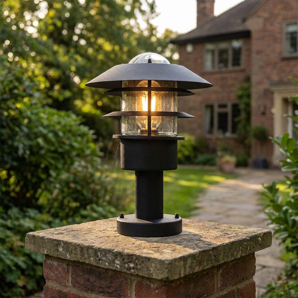 Modern black tiered garden lantern mounted on a brick pillar, illuminated in a garden setting.