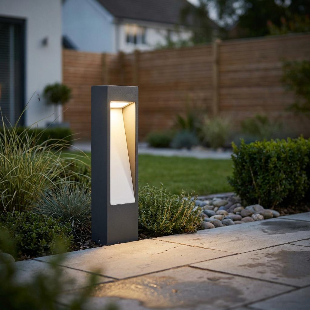 Modern dark grey bollard light with a warm glow illuminating a stone garden path.