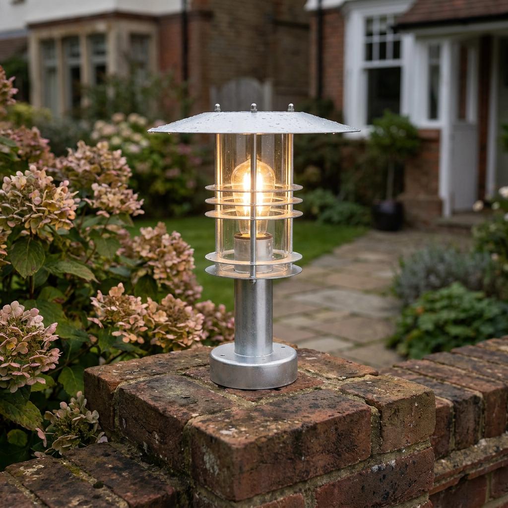 Galvanized steel pedestal lantern with a warm Edison bulb, mounted on a brick garden wall.
