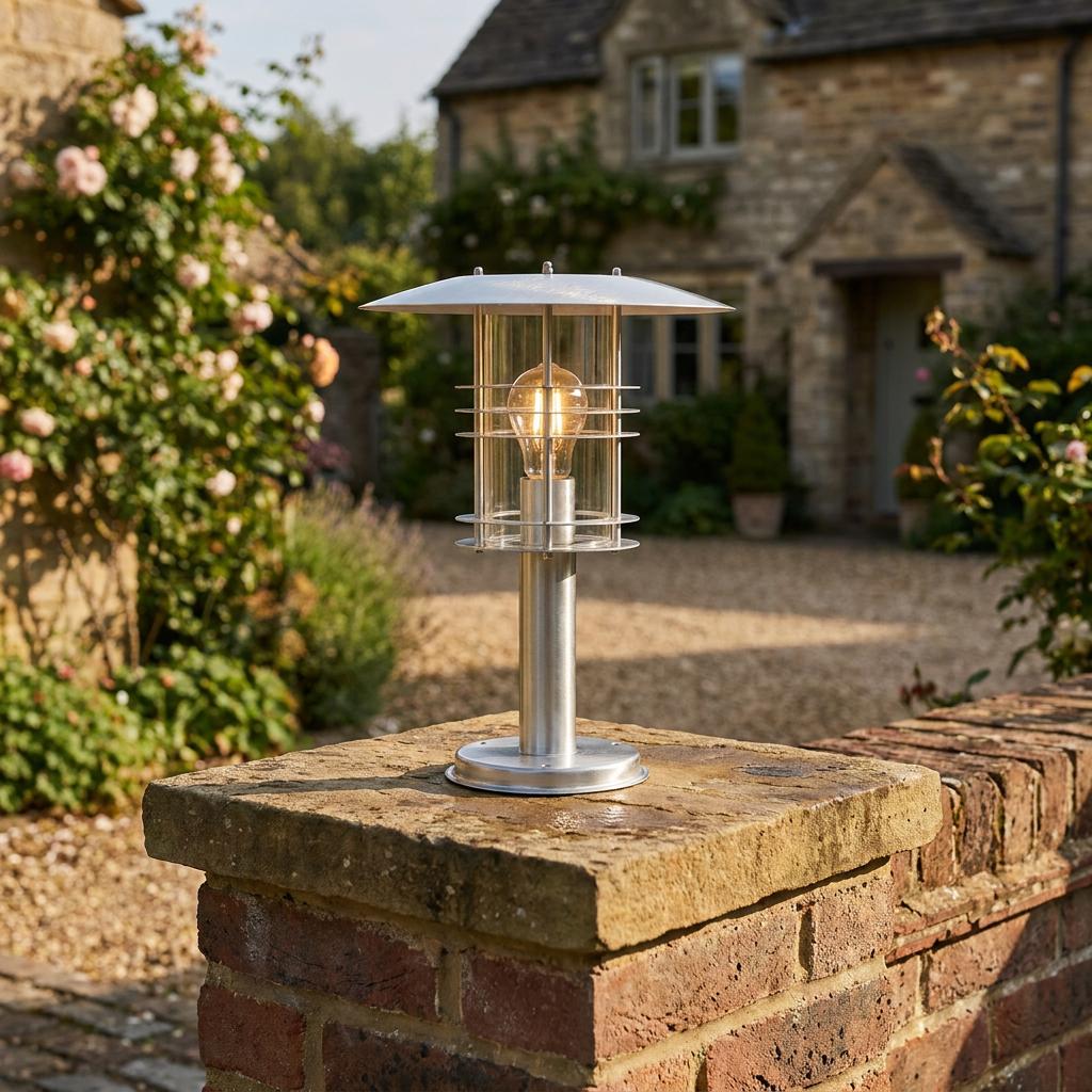 Modern stainless steel pillar light with a glowing filament bulb mounted on a stone garden wall.