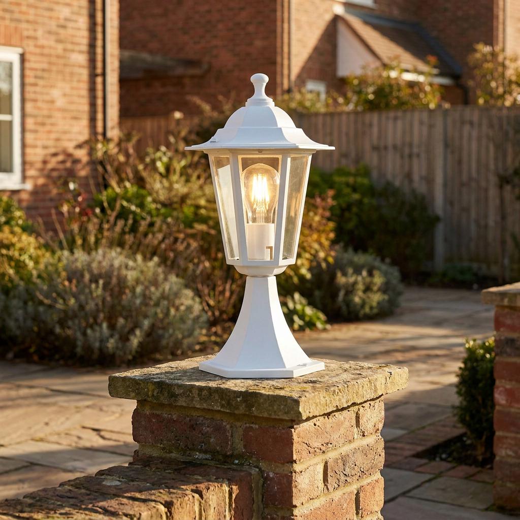 White outdoor lantern light fixture mounted on a brick pillar in a sunny garden setting.